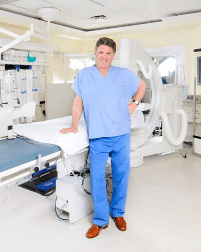 A male healthcare professional in scrubs stands confidently in a modern medical examination room.